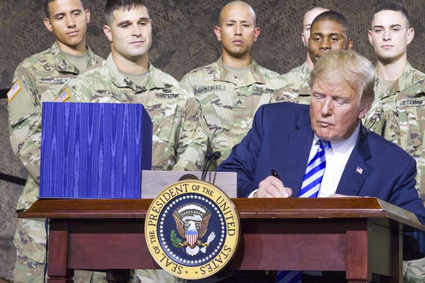 President Trump signs a bill at a small desk, with six US Army men behind him.
