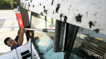 A man wipes bug splatters off the windshield of his large van; there are even more splatters above the windshield.