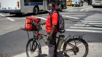 A Black Grubhub delivery driver with his bike who is visibly sweating