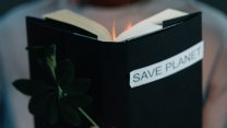 Someone holding a black book that says "save planet" on it. It's starting to become on fire