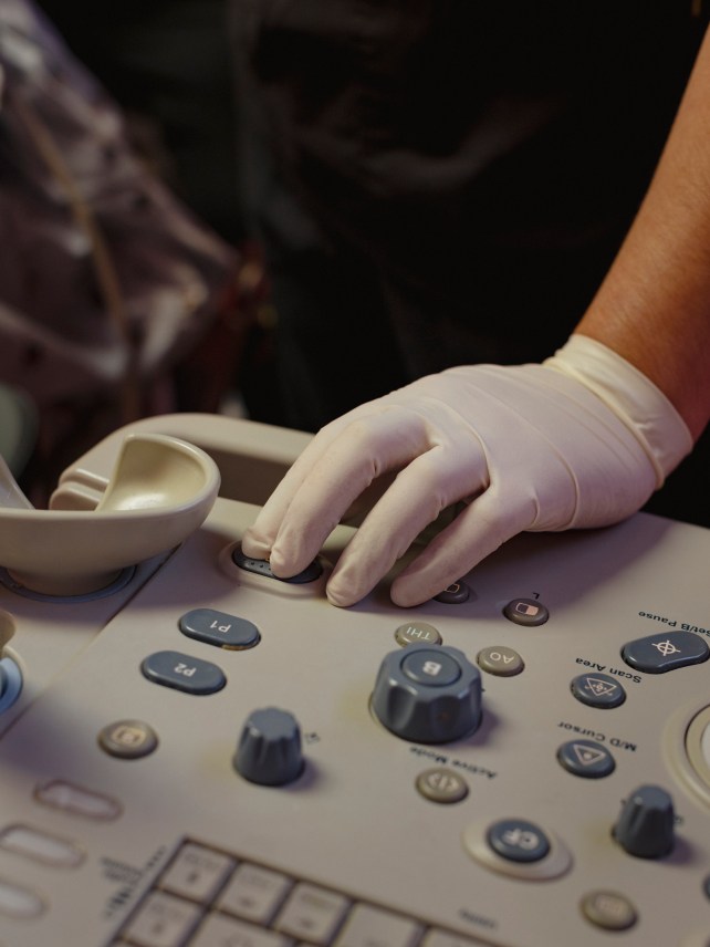 A hand of an operating room technician, conductsing an ultrasound during a procedure.