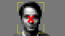 Man with pixelated features appears in the center of a gray background. Around his face is a rectangle made up of yellow lines, signifying a facial recognition program. There is a red "X" in the middle of the box, over the man's face.
