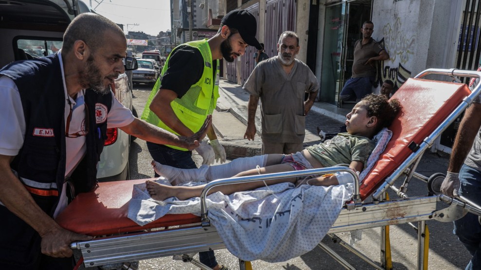 A child lying on a twisted sheet with a bandaged leg is unloaded from an ambulance on a stretcher.