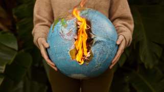 Someone with white hands holding a globe that is on fire