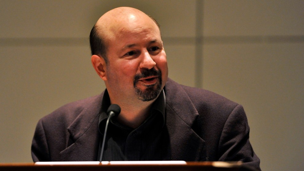 A white man with a mostly bald head speaks in front of a podium.