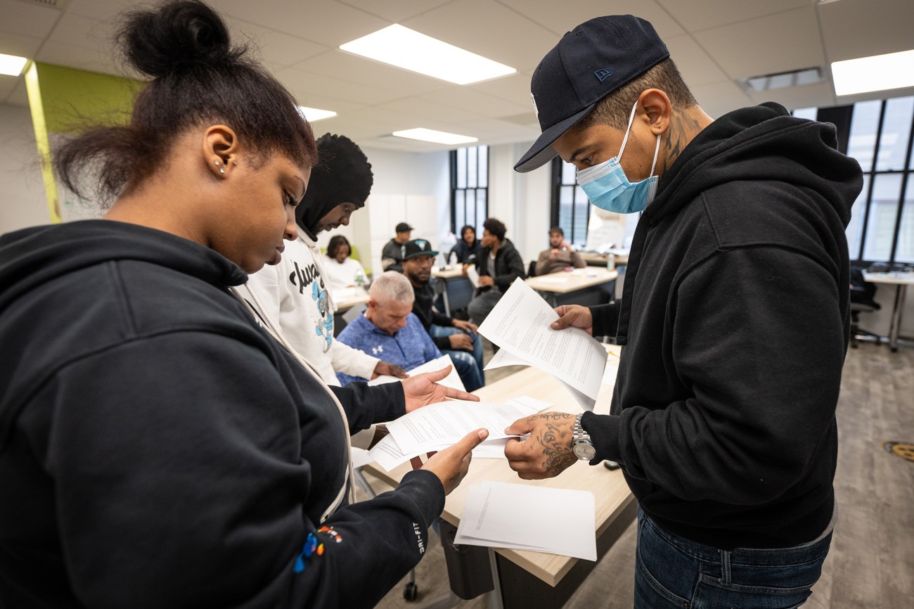 A man wearing a mask looks at papers with students.