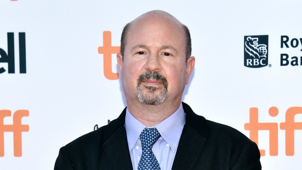 A man with a bald head and a blue tie stands in front of a white background.