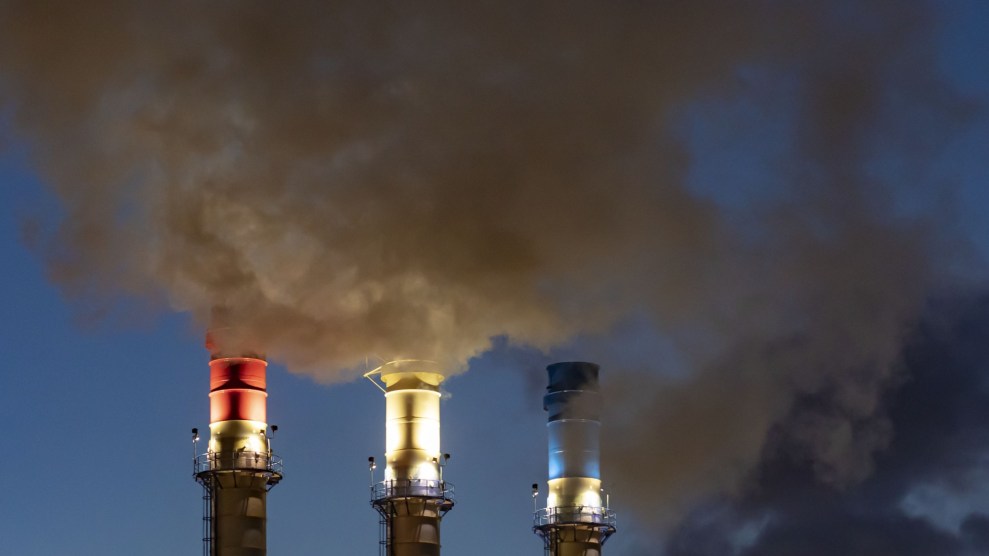 Three smoke stacks in the USA flag colors billow with grey smoke over a dark blue sky.