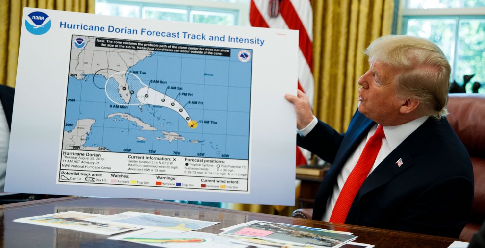 president trump sits in the oval office looking at a chart of a hurricane's path that has been drawn on with a sharpie