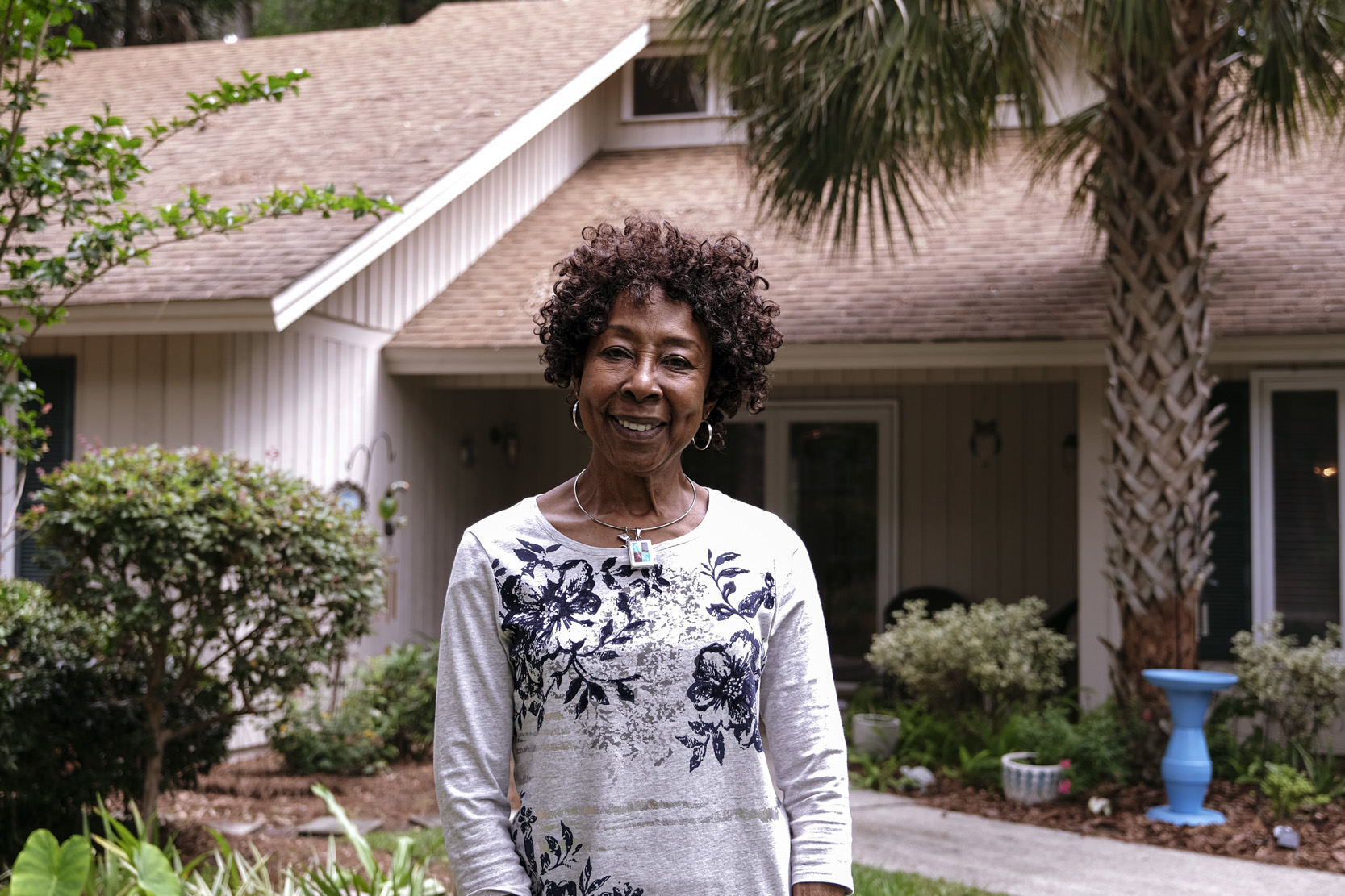 A woman smiling in front of a house with palm trees.
