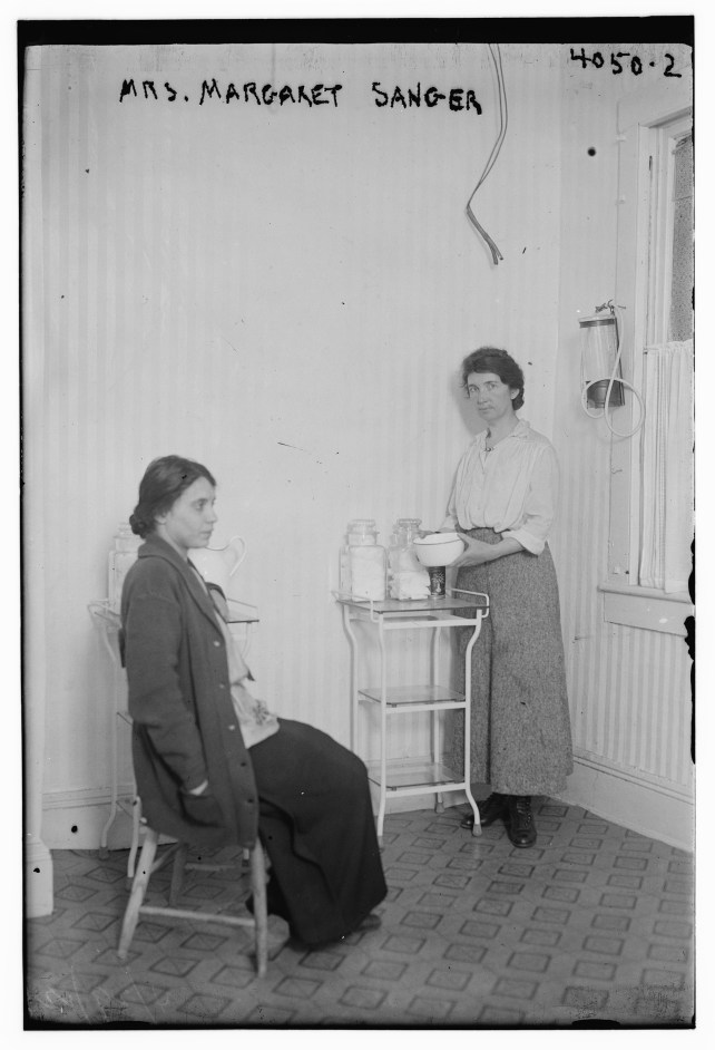 One woman sitting, another standing in an old doctor's office.