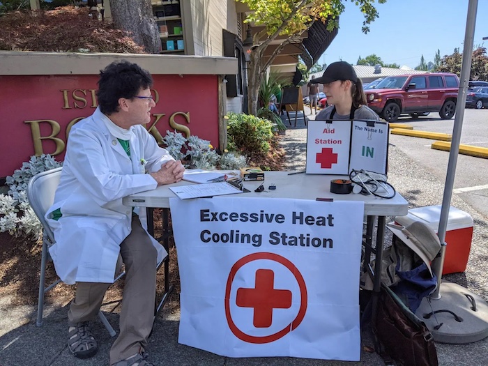 Two people sitting down at a table with a sign that says "excessive heat cooling station"