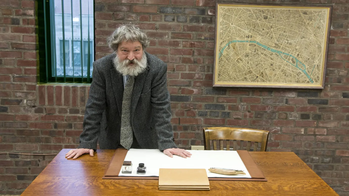 Portrait of bearded man standing, leaning over a desk.