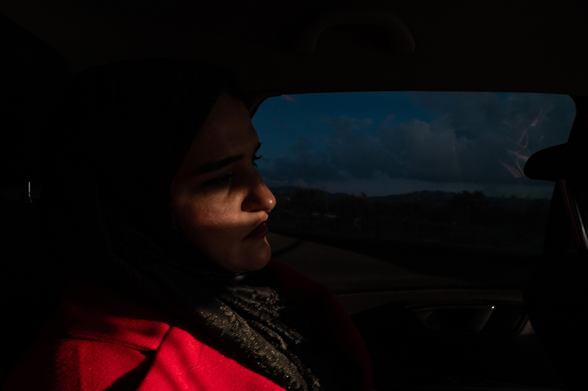 Dark photo of a woman sitting in a car with a streak of light across her face.