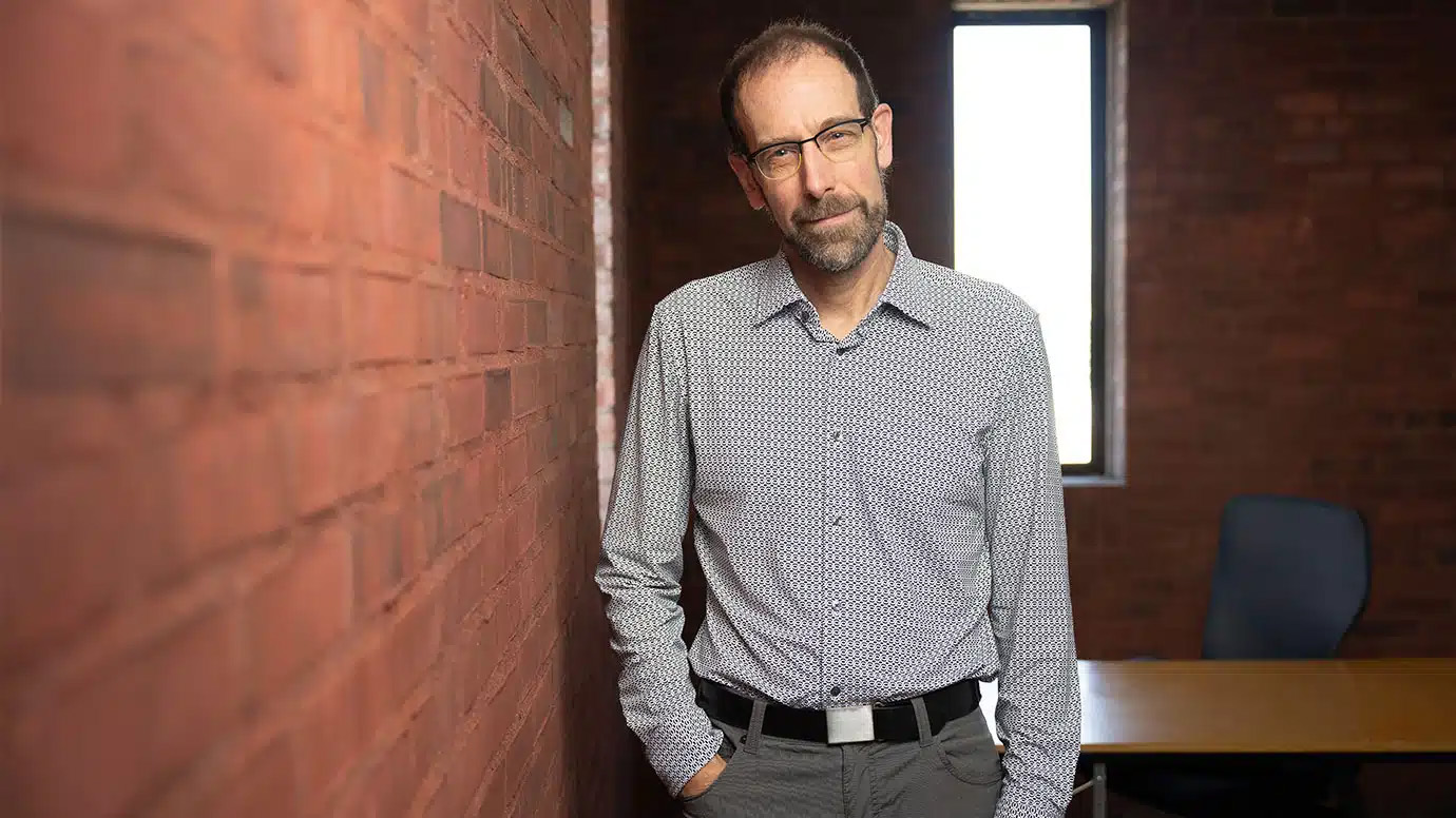 Portrait of bearded man standing next to a brick wall.