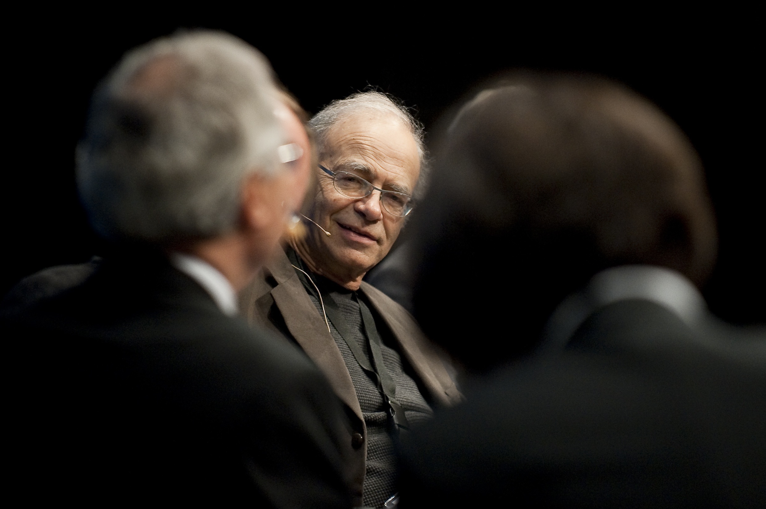 Peter Singer, wearing glasses, looks at two people with whom he is speaking.