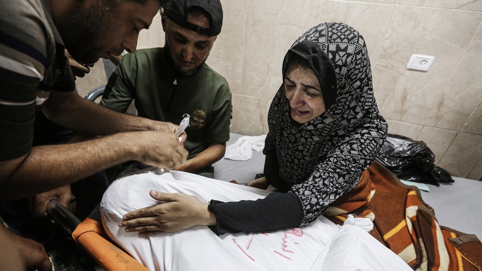 Woman crying over dead body wrapped in a white sheet.