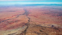 Light blue sky blends to an expansive, red and orange landscape with several winding streams