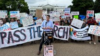 A large banner that says pass the torch behind a man speaking in front of the White House