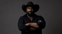 Portrait of black man wearing a black cowboy hat, with his arms crossed.