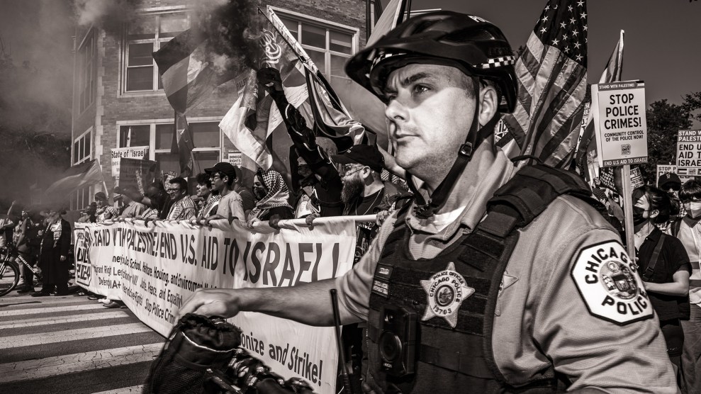 Black and white photo a crowd of Pro-Palestinian protestors holding a banner; in the foreground is an officer of the Chicago Police Department.