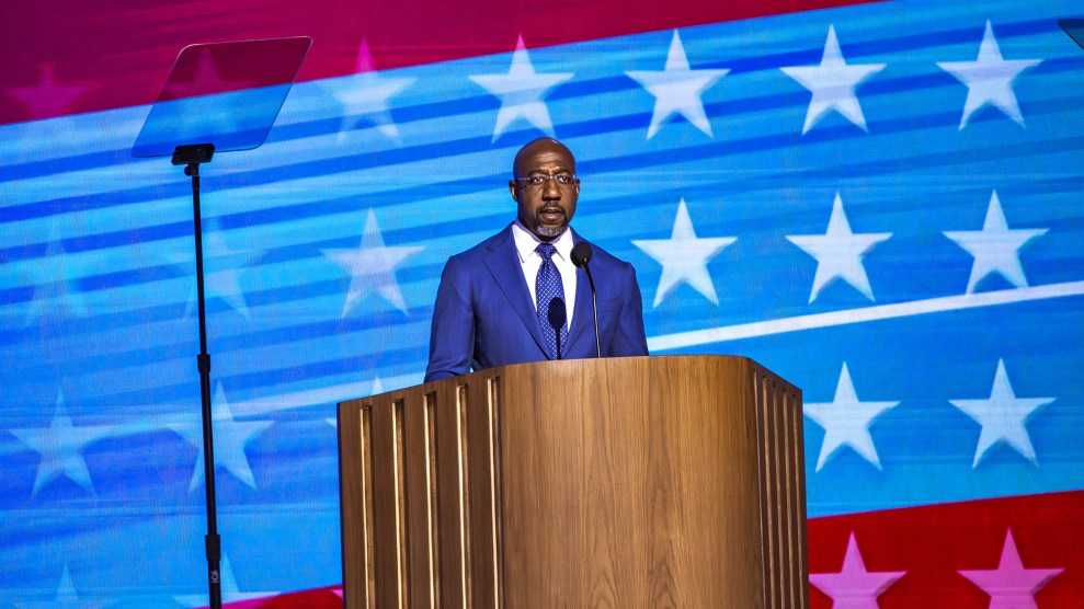 Senator Raphael Warnock standing at a lecturn with a digital American flag behind him.