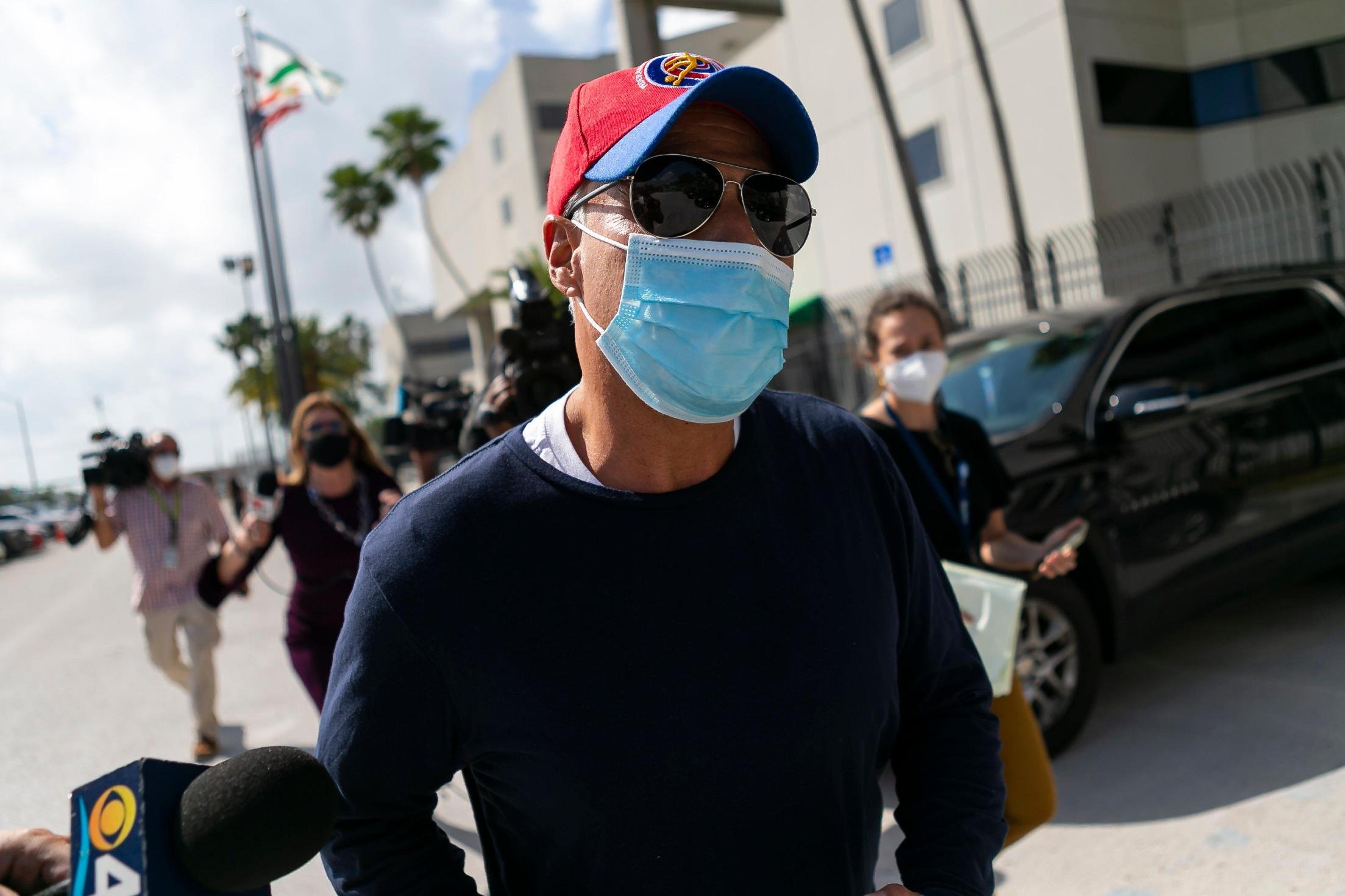 Man in mask, sunglasses and red baseball hat.