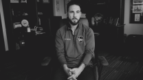 A black-and-white photo of Dearborn mayor Abdullah Hammoud sitting in his office, with a forsaken stare in his eyes. Hammoud is wearing a pullover emblazoned with a patch that reads: City of Dearborn, Michigan * Settled 1786 * Hometown of Henry Ford