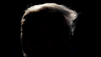 President Trump, his face obscured in dark shadow, talks with media while departing the White House en route to California, March 13, 2018