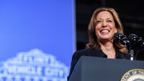 Kamala Harris smiling on stage in front of a microphone