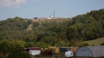 A natural gas well sits atop a hill above a quaint farm.