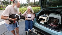 Two adults move their dog into a dog kennell as they evacuate.