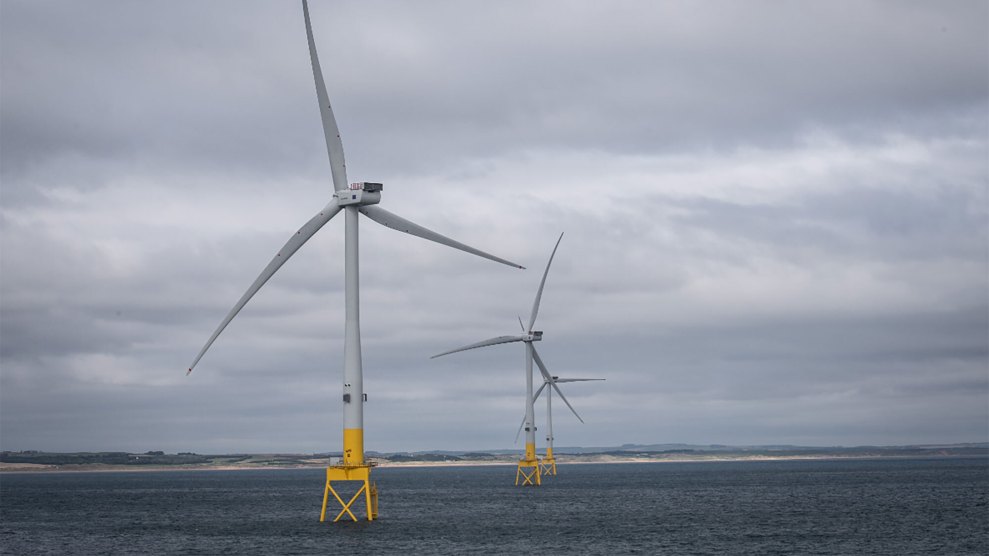 Two wind turbines on yellow stands in the ocean.