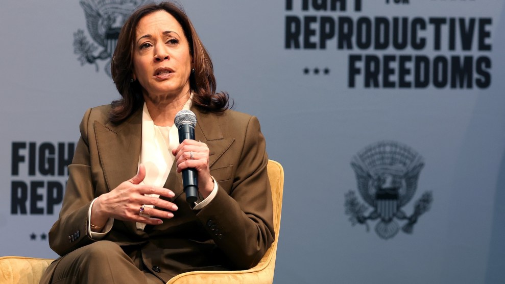 Kamala Harris, in a brown suit, sits in a yellow chair holding a microphone in front of a background reading "Fight for Reproductive Freedoms"