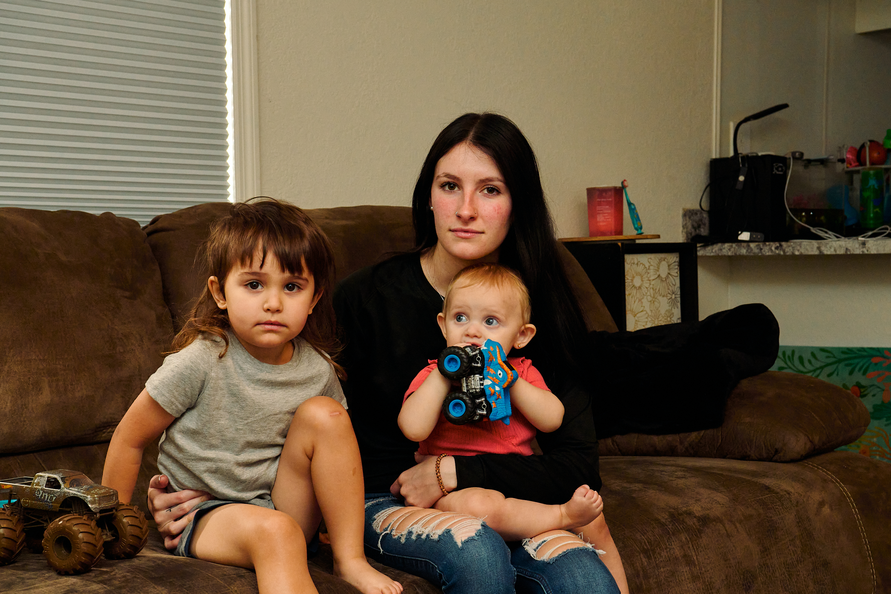 A woman sitting on a couch with one child in her lap and another sitting next to her.