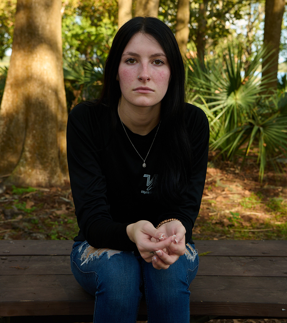 Portrait of woman sitting on a bench outside, looking at the camera.