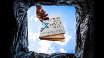 A hand drops a book titled, "The Case For Israel" into a trash can