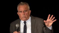 RFK Jr. speaking onstage in a suit with a microphone