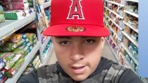 A young latino man in a red baseball cap looking into his phone camera and talking while inside what looks like a grocery store