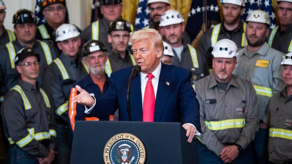 Trump, wearing a red tie, stands at a podium in front of miners wearing safety gear.