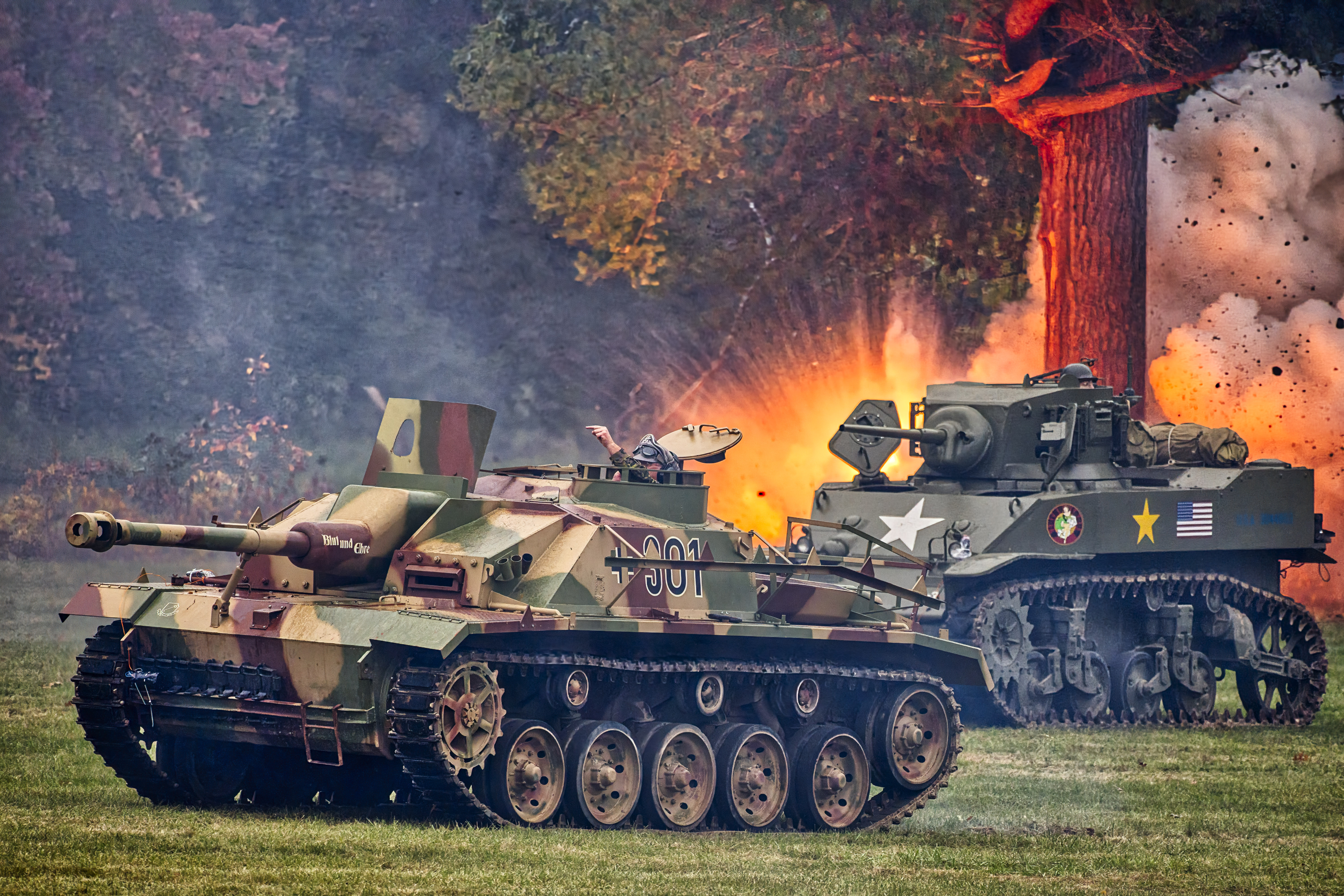 Two tanks in a field with an explosion behind the second tank.