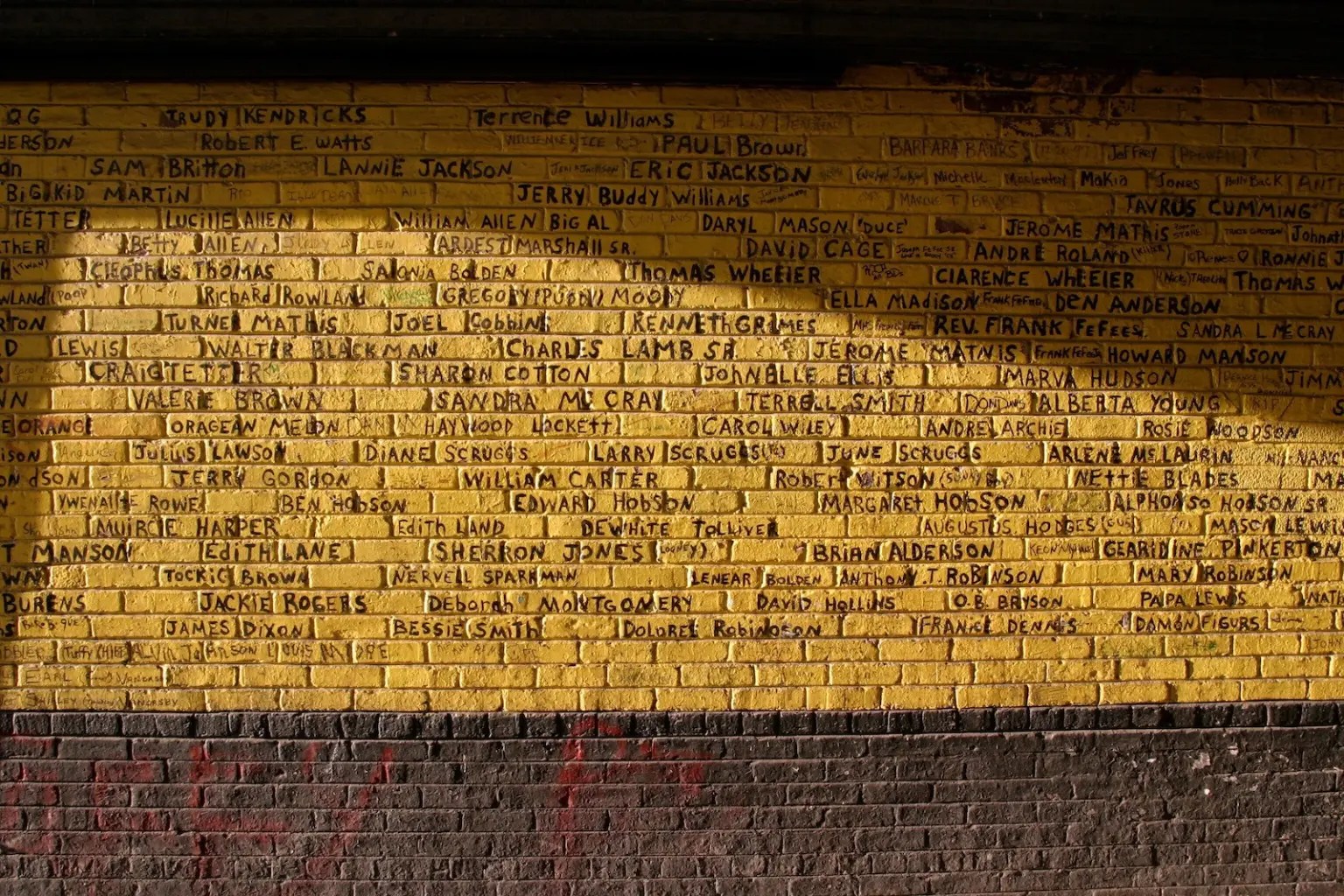 A yellow wall covered in names written in black.