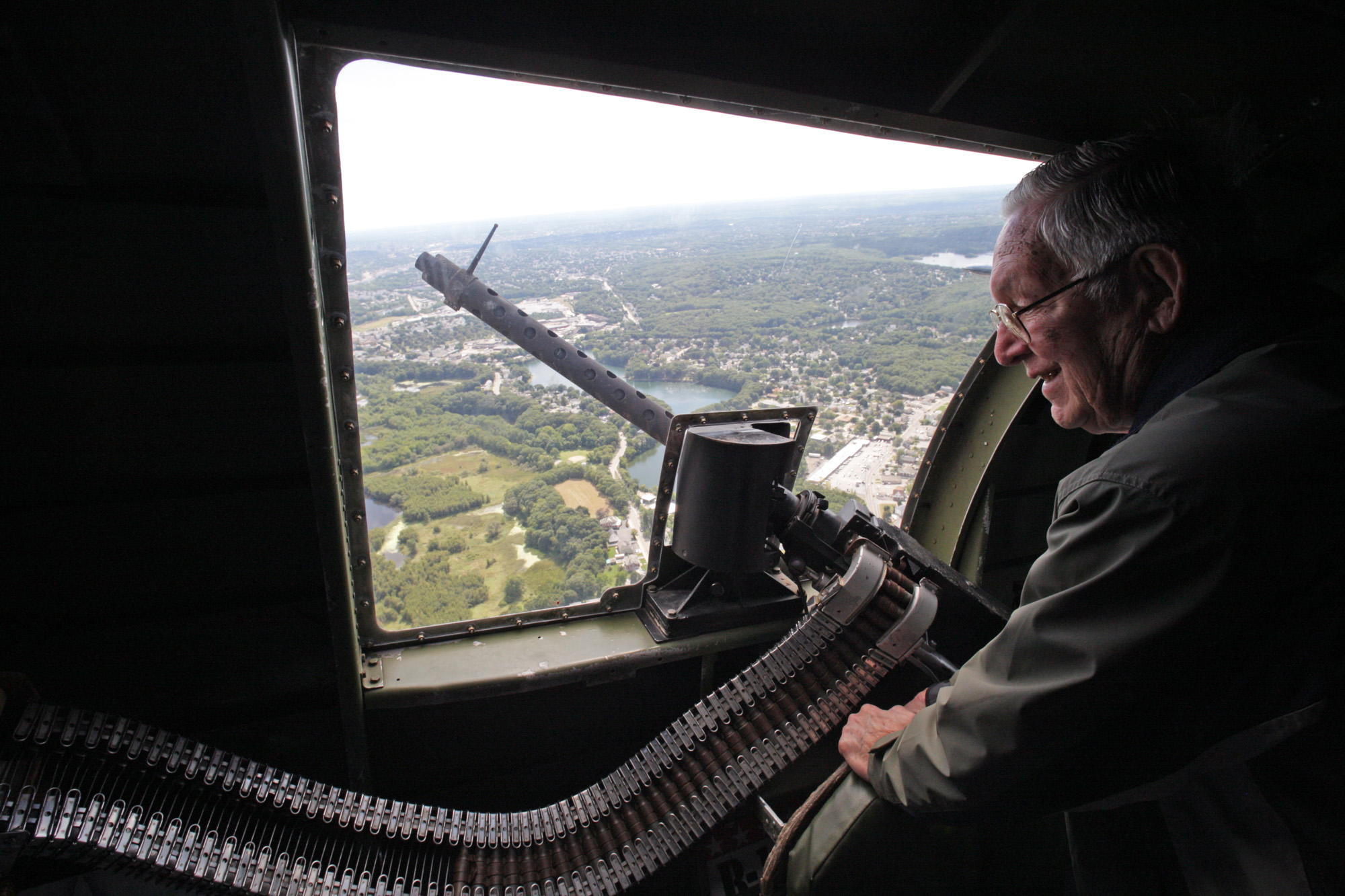 Man sitting at window of fighter plane in flight with a machine gun pointed out the window.