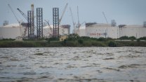 Large white liquid natural gas tanks surrounded by cranes are seen from across a river