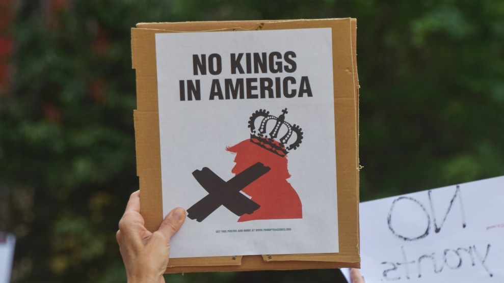 a hand holding up a sign that says "No Kings in America" with an illustration of a Trump figure wearing a crown with an X over it