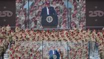 Donald Trump on stage in front of a crowd of soldiers, with a big screen showing him in the background