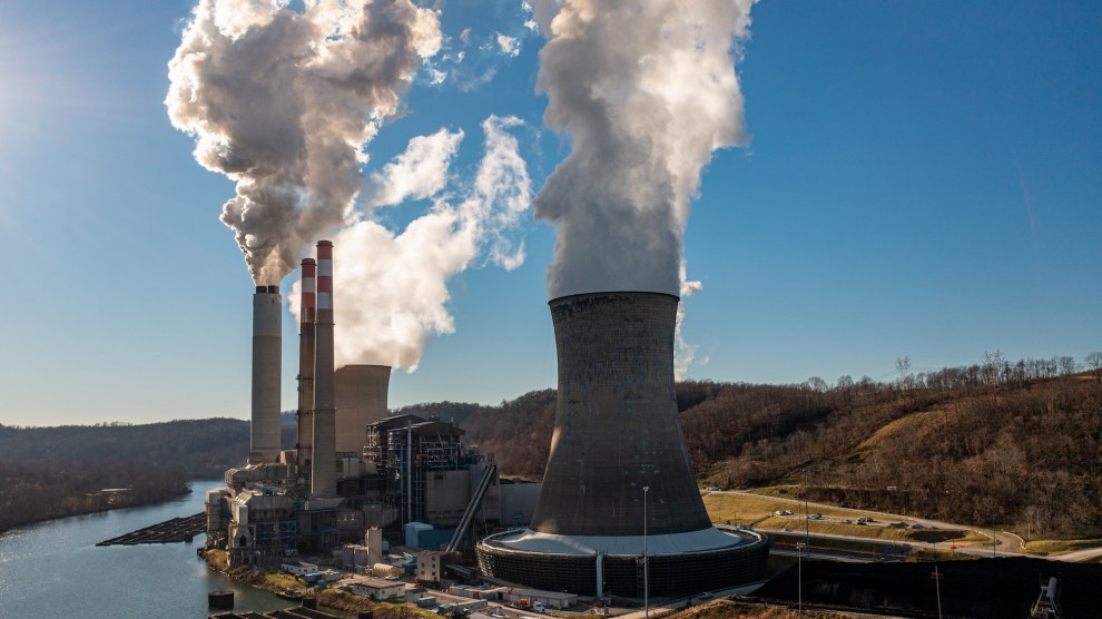 Smokestacks with emission plumes set against a blue sky at the water's edge.