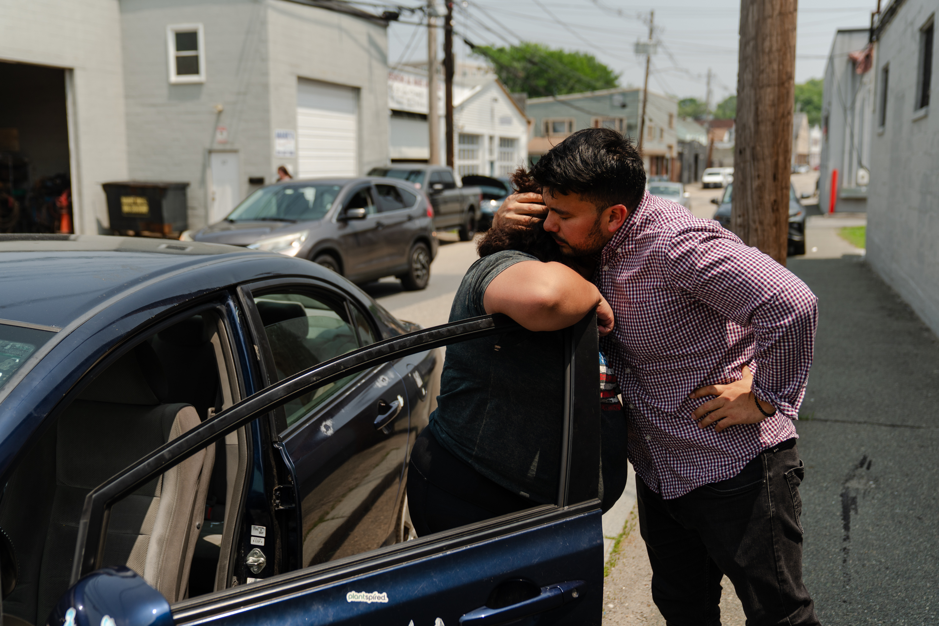 Man and woman hugging next to a car's open driver-side door.