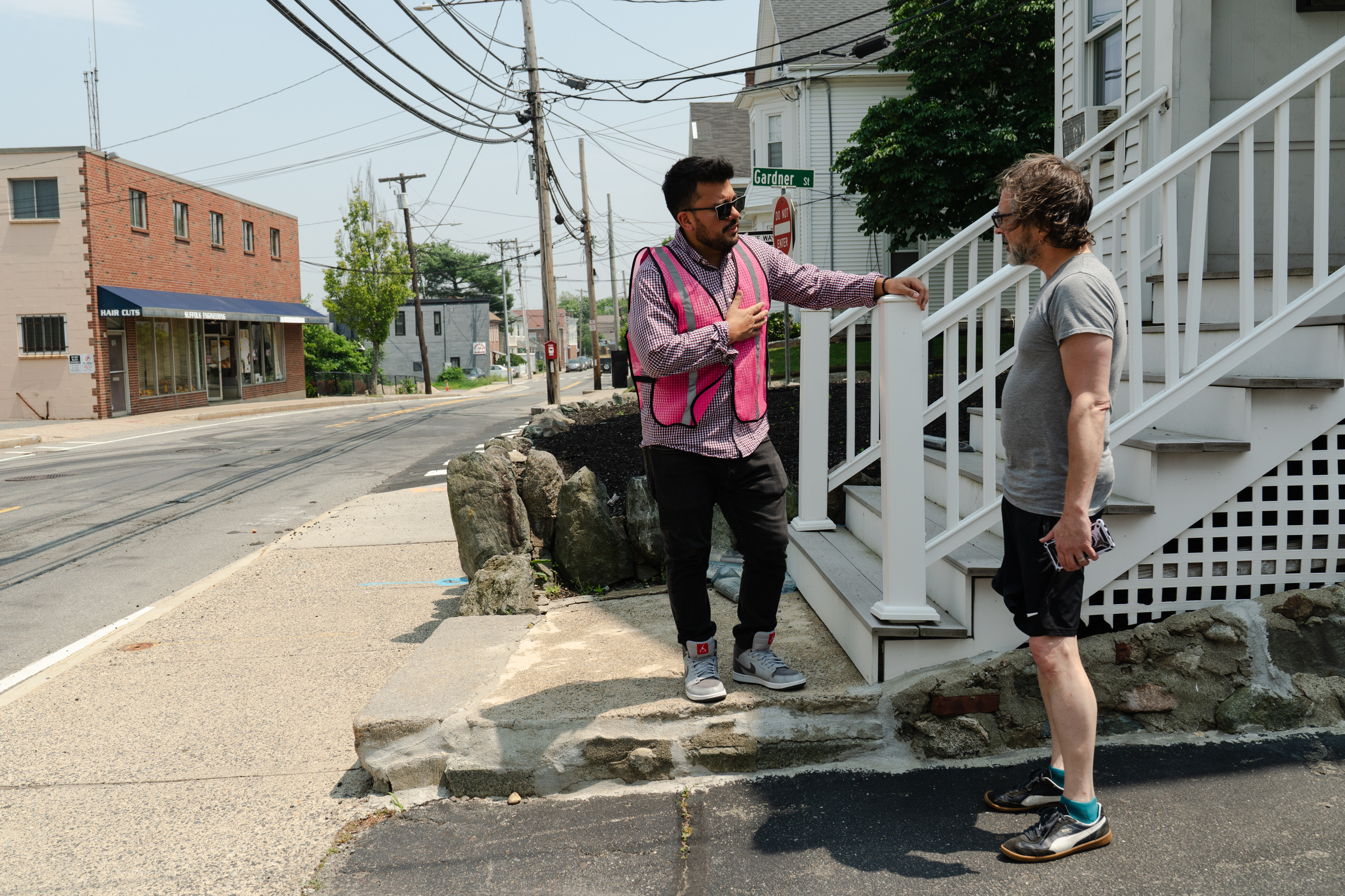 Two men talk on the front steps leading to a house.