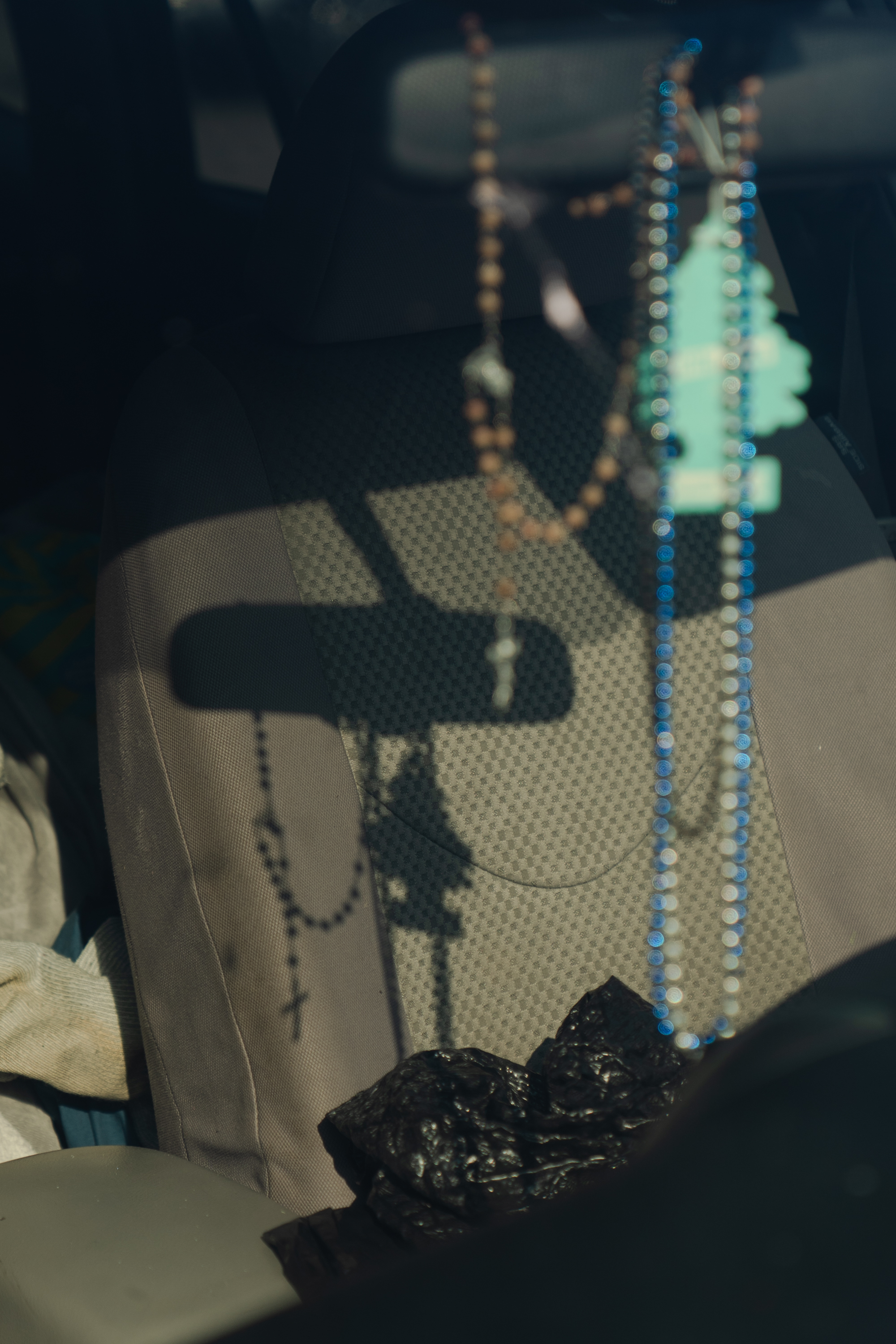 A set of rosary beads hanging from the rearview mirror in a car casts a shadow onto the driver's seat.
